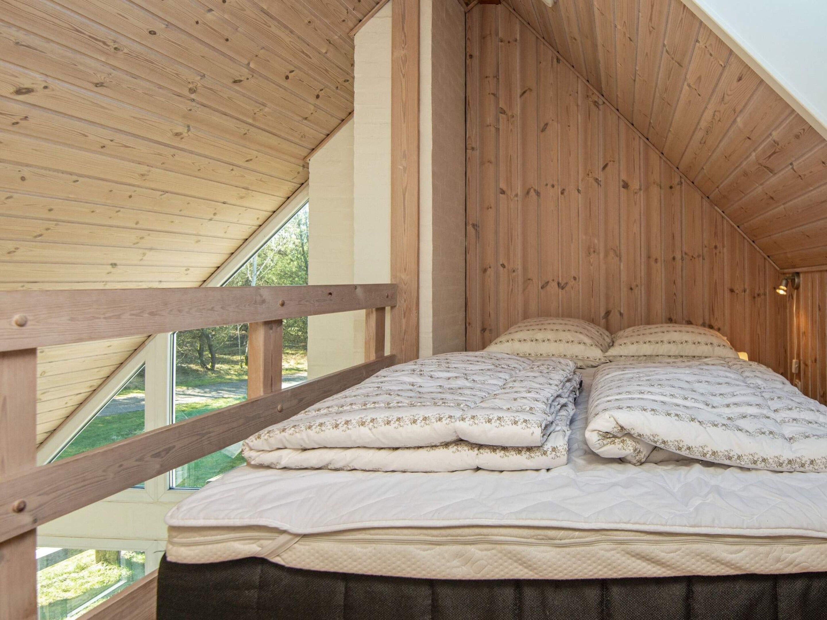 A bedroom with a wooden ceiling, a bed with multiple pillows, and a window.