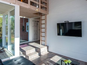 A modern living room with a TV mounted on the wall, a sofa, and a staircase leading to an upper level. - 4 Star Holiday Home in Romo (Rømø)
