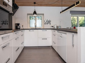 A modern kitchen with white cabinets, a black pendant light, and a window with a view of trees. - 4 Star Holiday Home in Romo (Rømø)