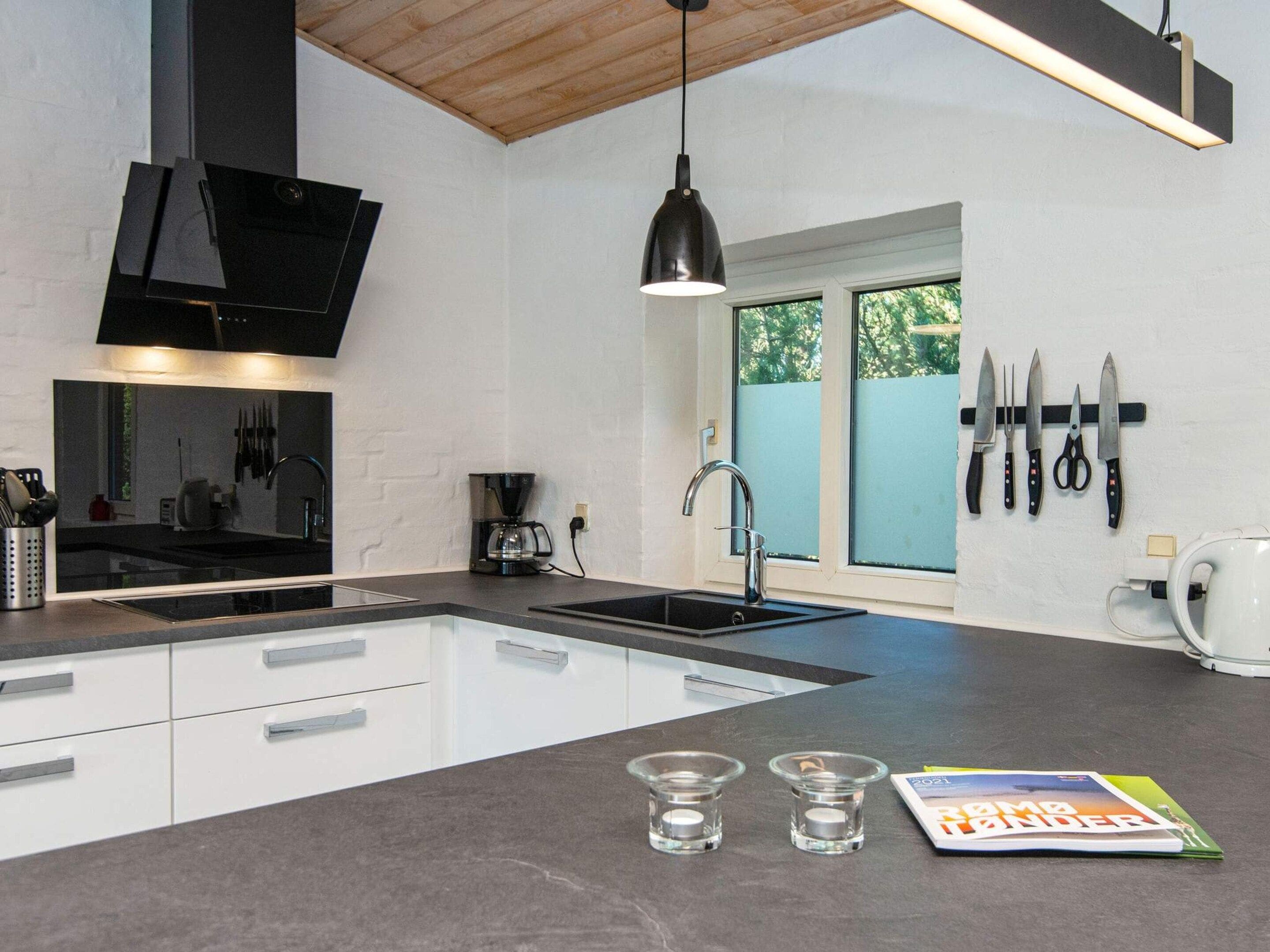 A modern kitchen with a black countertop, white cabinets, a coffee maker, a sink, and a window with a view of trees.