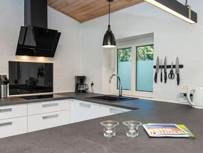 Cocina moderna con encimera negra, armarios blancos, cafetera, fregadero y ventana con vista a árboles.