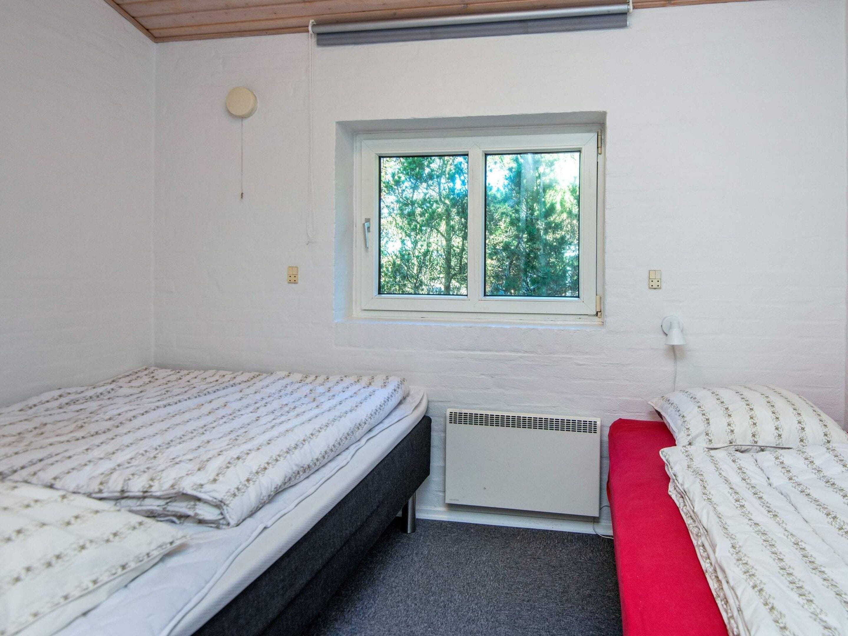 A room with two beds, a window, a wall-mounted heater, and a power outlet.