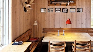 A wooden interior with a wooden table and benches, framed pictures on the wall, and a mounted fish.