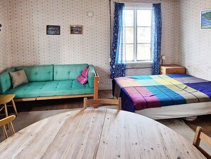 A room with a green sofa, a bed with a multicolored quilt, a wooden table, and a window with blue curtains. - 4 Person Holiday Home in Malung-by Traum (Malung)