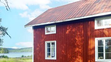 A red wooden house with a metal roof, two windows, and a chimney.