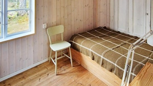 A small, single-bed room with wooden walls and a window.