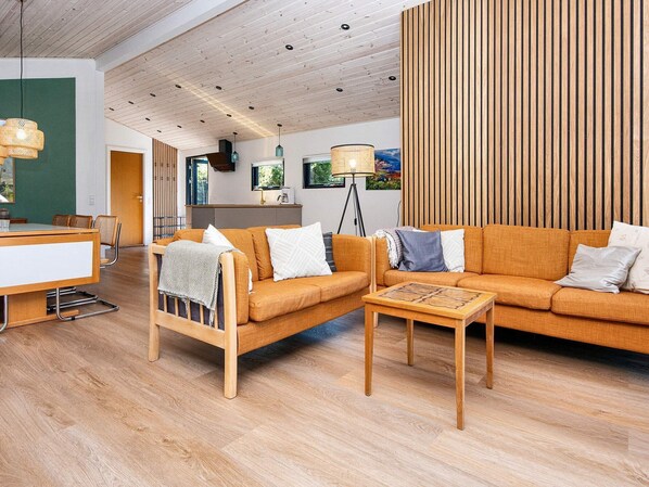 A modern living room with a wooden floor, a sofa, a coffee table, and a dining area with a table and chairs. - 6 Person Holiday Home in Glesborg (Glesborg)
