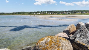 Une plage côtière avec une eau claire, des rochers et des maisons en arrière-plan.