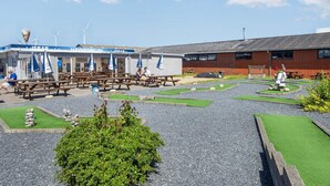 Un café en bord de mer avec une terrasse, une éolienne en arrière-plan et un petit jardin.