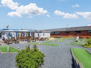 A seaside café with outdoor seating, a wind turbine in the background, and a small garden area.
