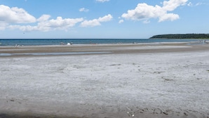 Une plage avec une vaste étendue de sable, une mer calme et, au loin, une colline boisée.