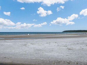 A beach with a wide sandy area, a calm sea, and a forested hill in the distance.