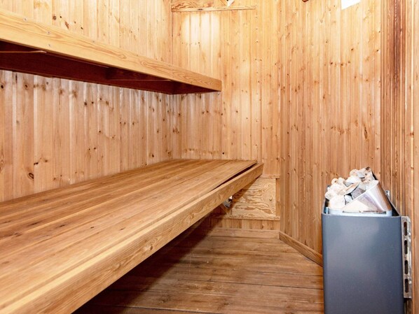 Un sauna en bois, doté de bancs et d’un récipient en métal.