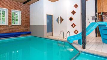 Piscina interna com um escorregador azul, parede de tijolos e teto de madeira.