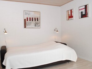 Una habitación minimalista con una cama individual, dos lámparas de pared y dos obras de arte enmarcadas.