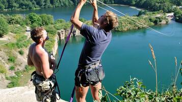 Twee personen bereiden zich voor op een zipline-activiteit, met een schilderachtige rivier en een bebost landschap op de achtergrond.