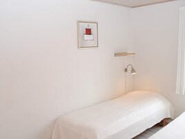 Ein kleiner, schlichter Raum mit einem Bett, einem Nachttisch, einer Lampe und einem gerahmten Bild an der Wand.