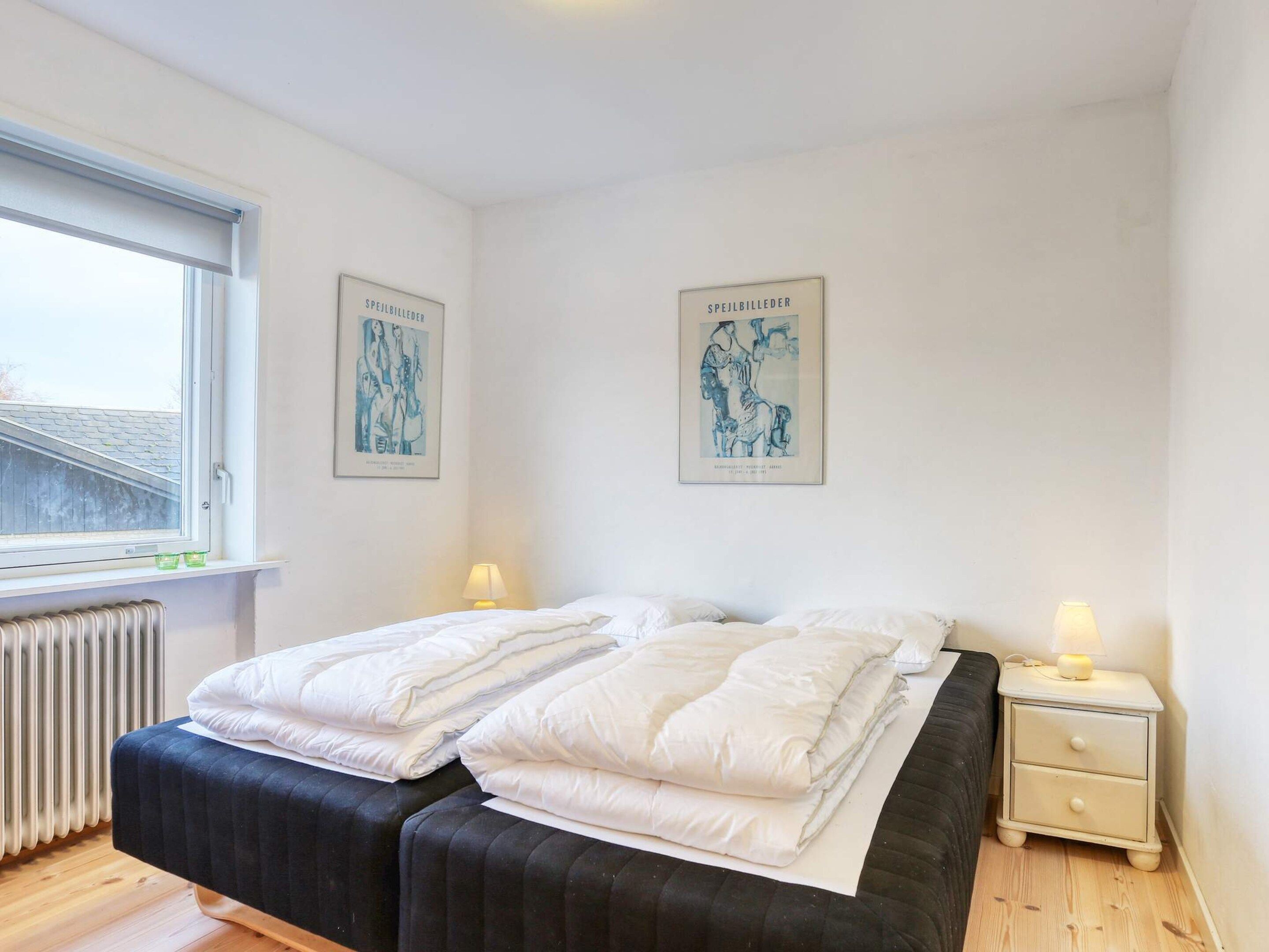 A bedroom with a bed, two bedside tables, a radiator, and two wall-mounted lamps.