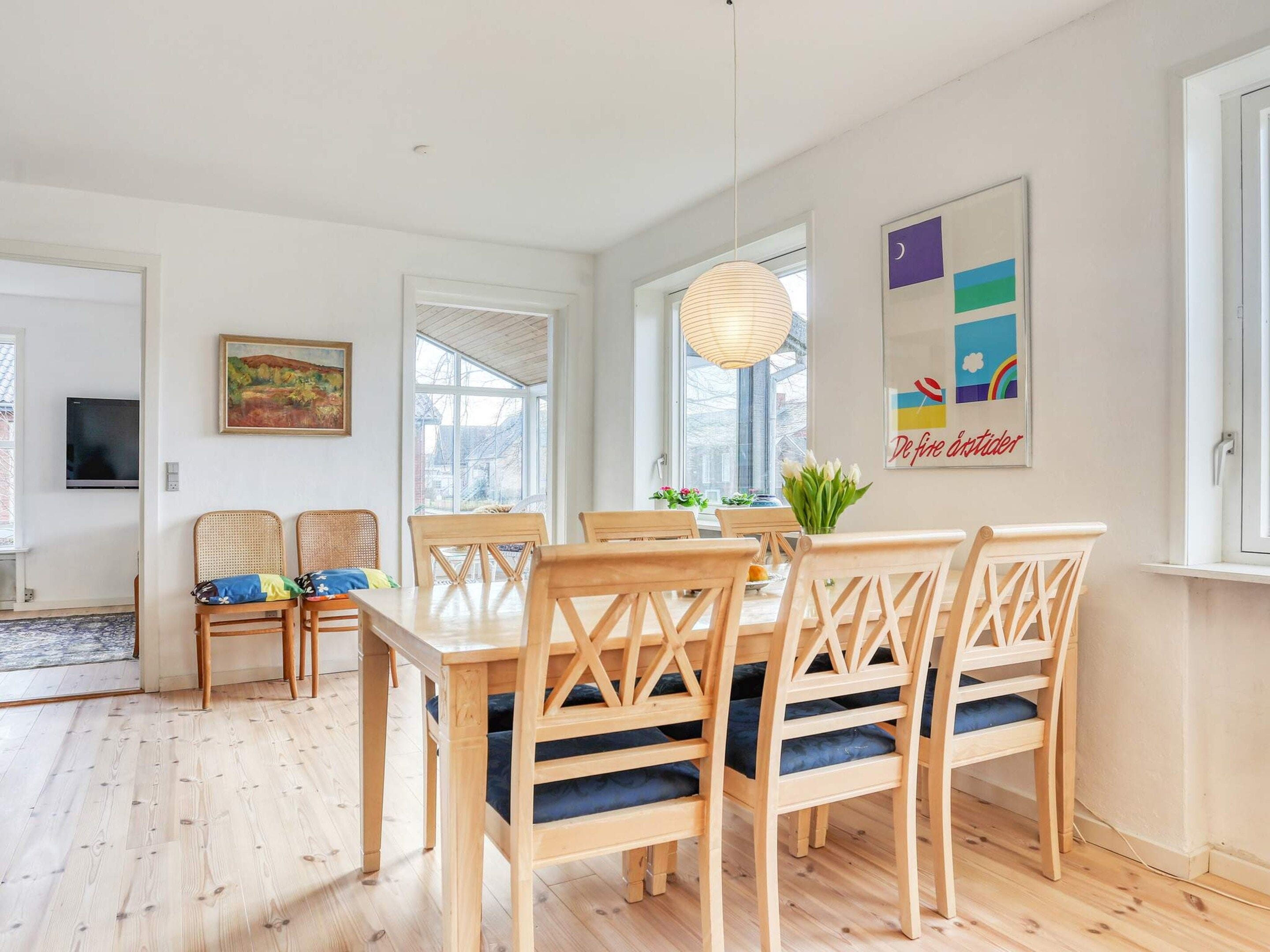A dining area with a wooden table and chairs, a hanging light fixture, and a window with a view.
