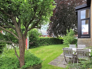 A garden with a wooden bench and table, surrounded by greenery and a tree. - 6 Person Holiday Home in Strandby (Strandby)