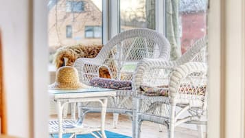 Wicker furniture with cushions, a blue rug, and a view of buildings through large windows.