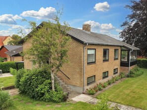 A two-story house with a brick facade, a chimney, and a small garden with a tree and flowers. - 6 Person Holiday Home in Strandby (Strandby)