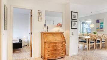 Una habitación con un aparador de madera, una mesa de comedor con sillas y una cama en la habitación contigua.