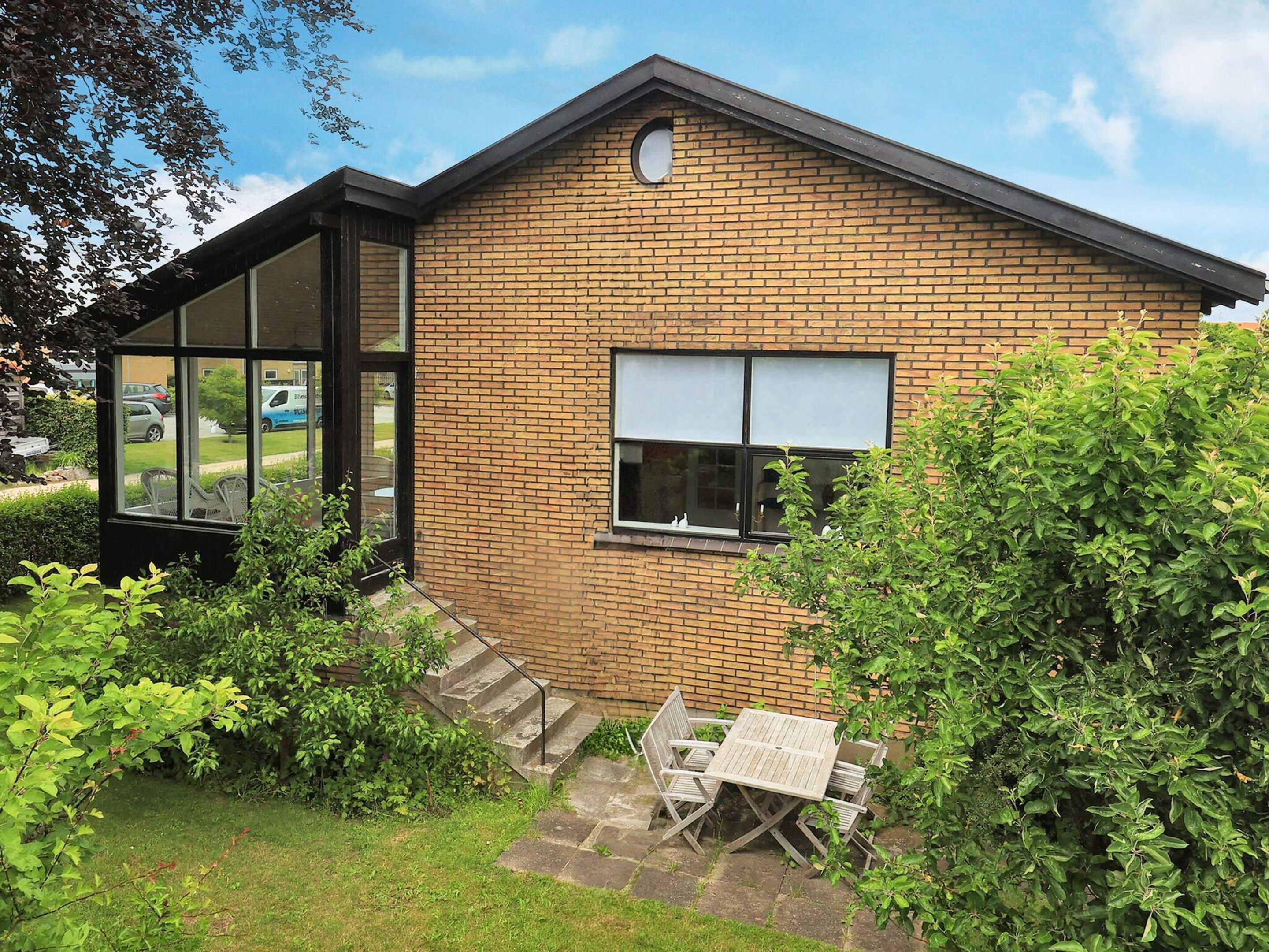 A brick house with a glass door, a small patio with a table and chairs, and a window with blinds.