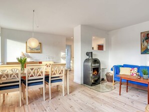 A modern living room with a wooden dining table, blue sofa, and a wood-burning stove. - 6 Person Holiday Home in Strandby (Strandby)