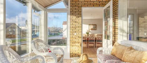 Una habitación luminosa con muebles de mimbre, un comedor y vistas a través de amplios ventanales.