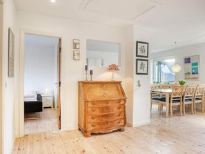 A room with a wooden dresser, a dining table with chairs, and a bed in the adjacent room. - 6 Person Holiday Home in Strandby (Strandby)