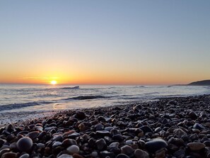 Uma praia com pedras e o sol se pondo sobre a água.