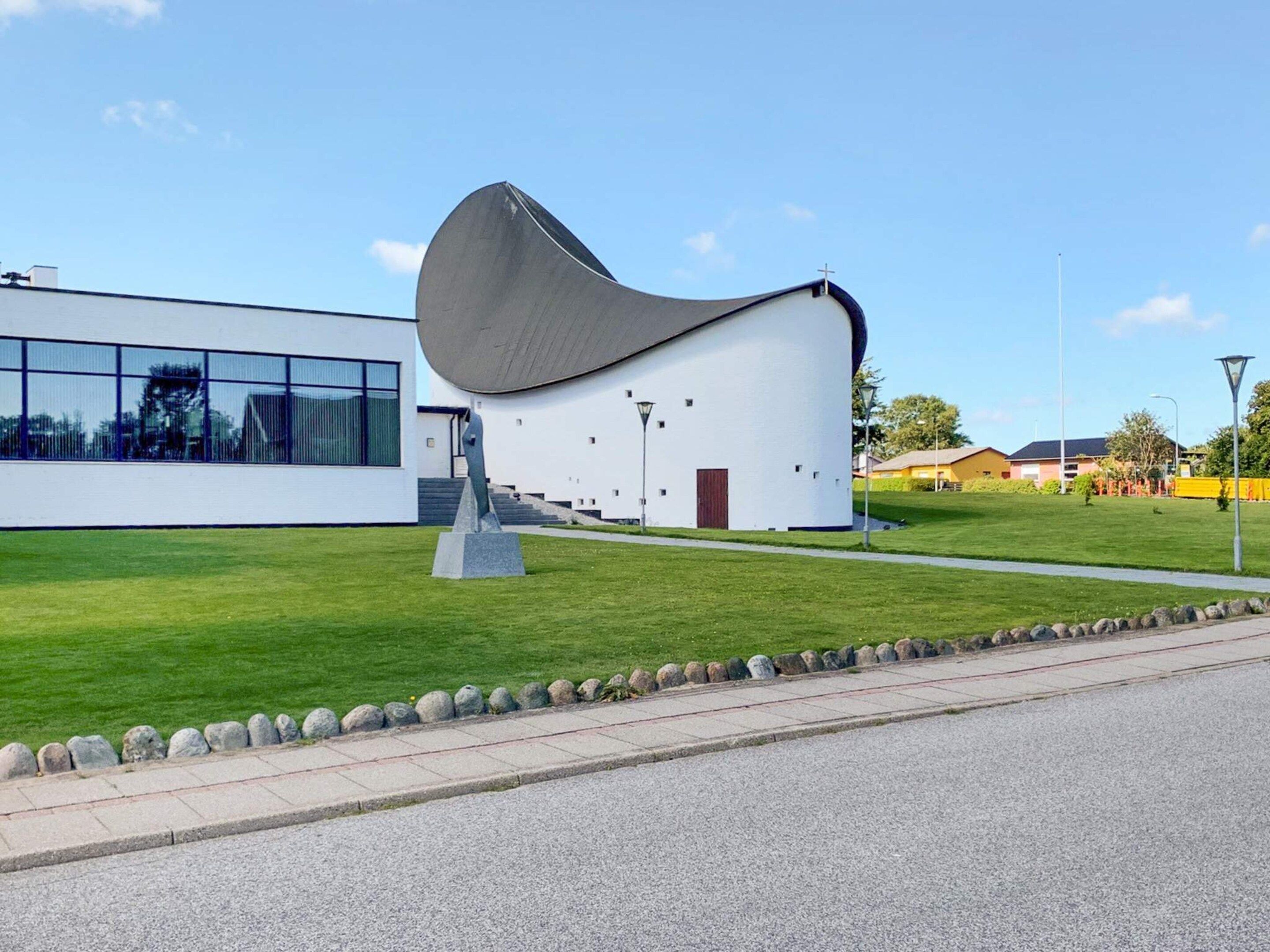 A modern building with a unique curved roof, a clear glass facade, and a well-maintained lawn.