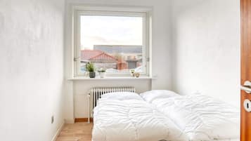 A small, bright room with a bed, a radiator, and a window overlooking a residential area.