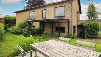 A two-story brick house with a covered patio and a wooden table and bench in the yard.
