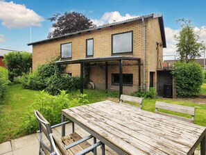 A two-story brick house with a covered patio and a wooden table and bench in the yard. - 6 Person Holiday Home in Strandby (Strandby)