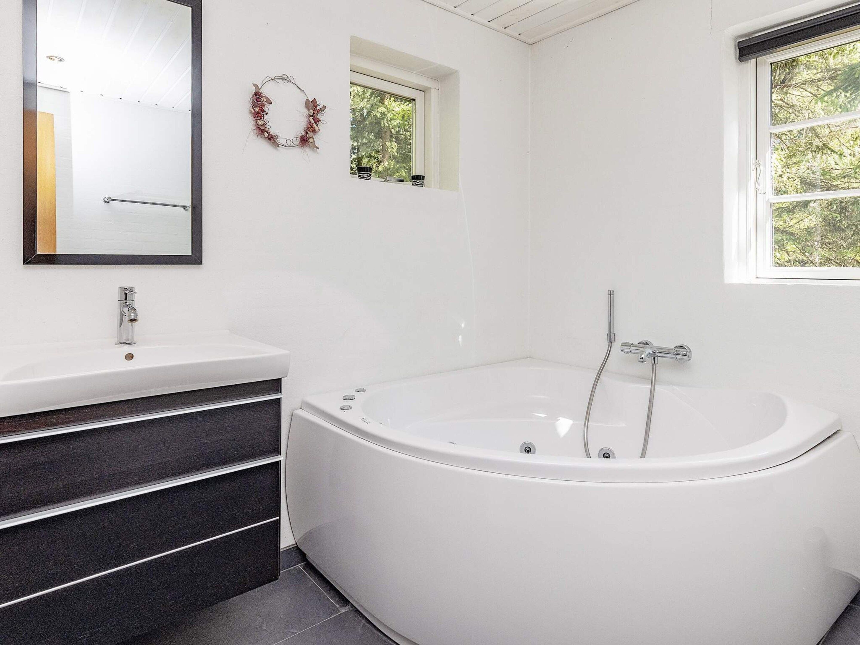 Un baño moderno con una bañera independiente, un espejo grande y un ventanal con vistas a árboles.