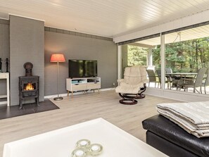 Ein modernes Wohnzimmer mit Kamin, Fernseher, einem bequemen Sessel und einem Essbereich mit Blick ins Freie.