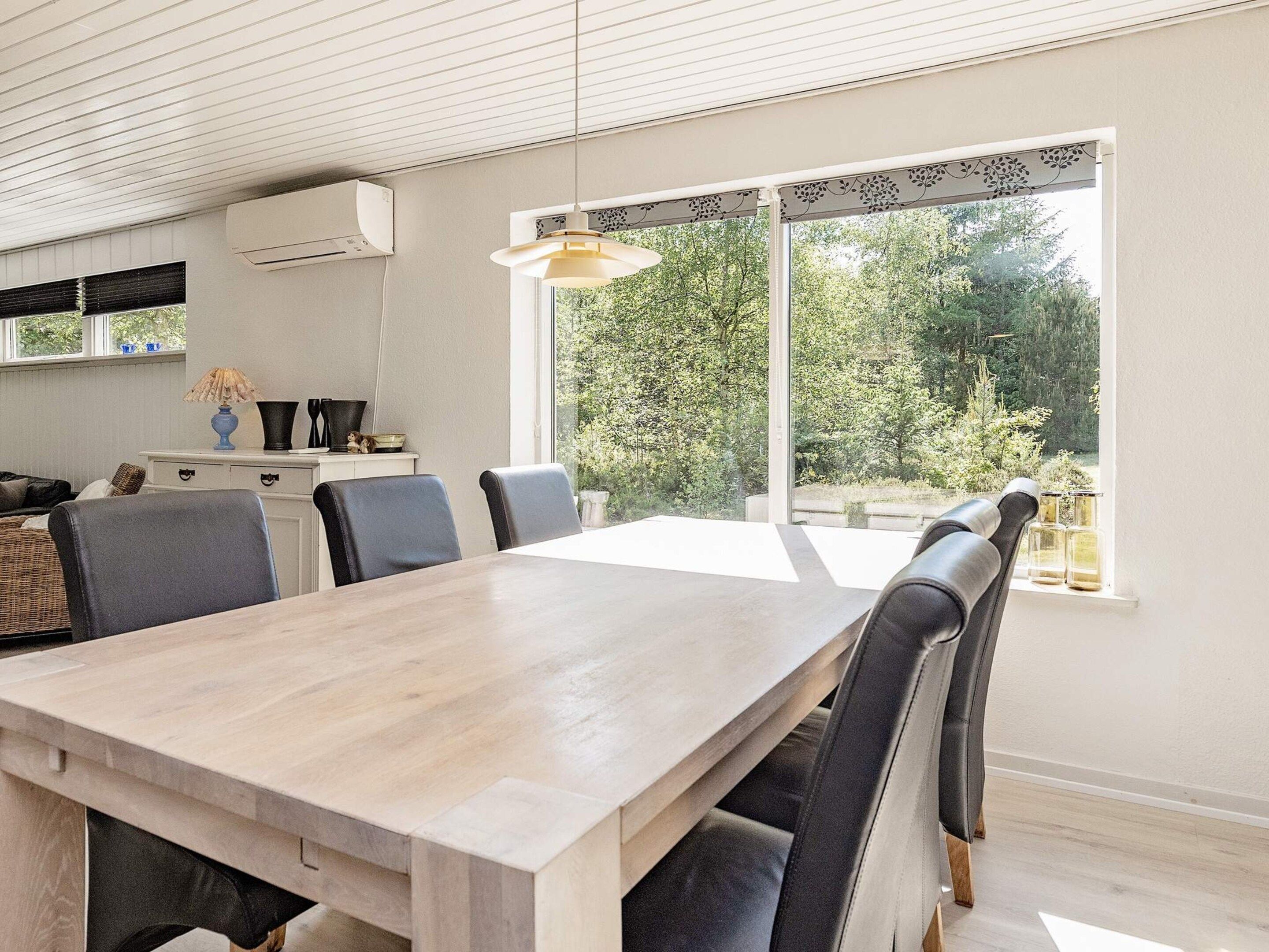 Un comedor moderno con una mesa y sillas de madera, una lámpara colgante y vistas a zonas verdes al exterior.