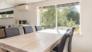 Un comedor moderno con una mesa y sillas de madera, una lámpara colgante y vistas a zonas verdes al exterior.