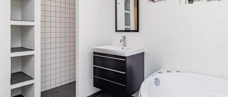 A modern bathroom with a white sink, a large mirror, a bathtub, and a shower area.