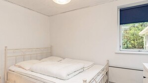 A single bed with a metal frame and white bedding in a room with white walls and a window with a view of trees. - 6 Person Holiday Home in Hojslev (Hojslev)