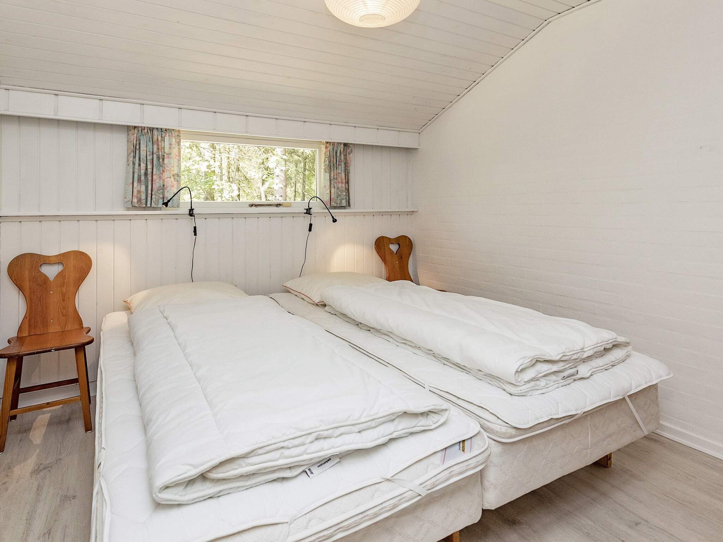 Una habitación con dos camas, una ventana con cortinas y una silla de madera.