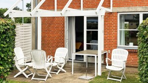 Une terrasse avec des chaises blanches et une table, une maison en briques et une fenêtre.