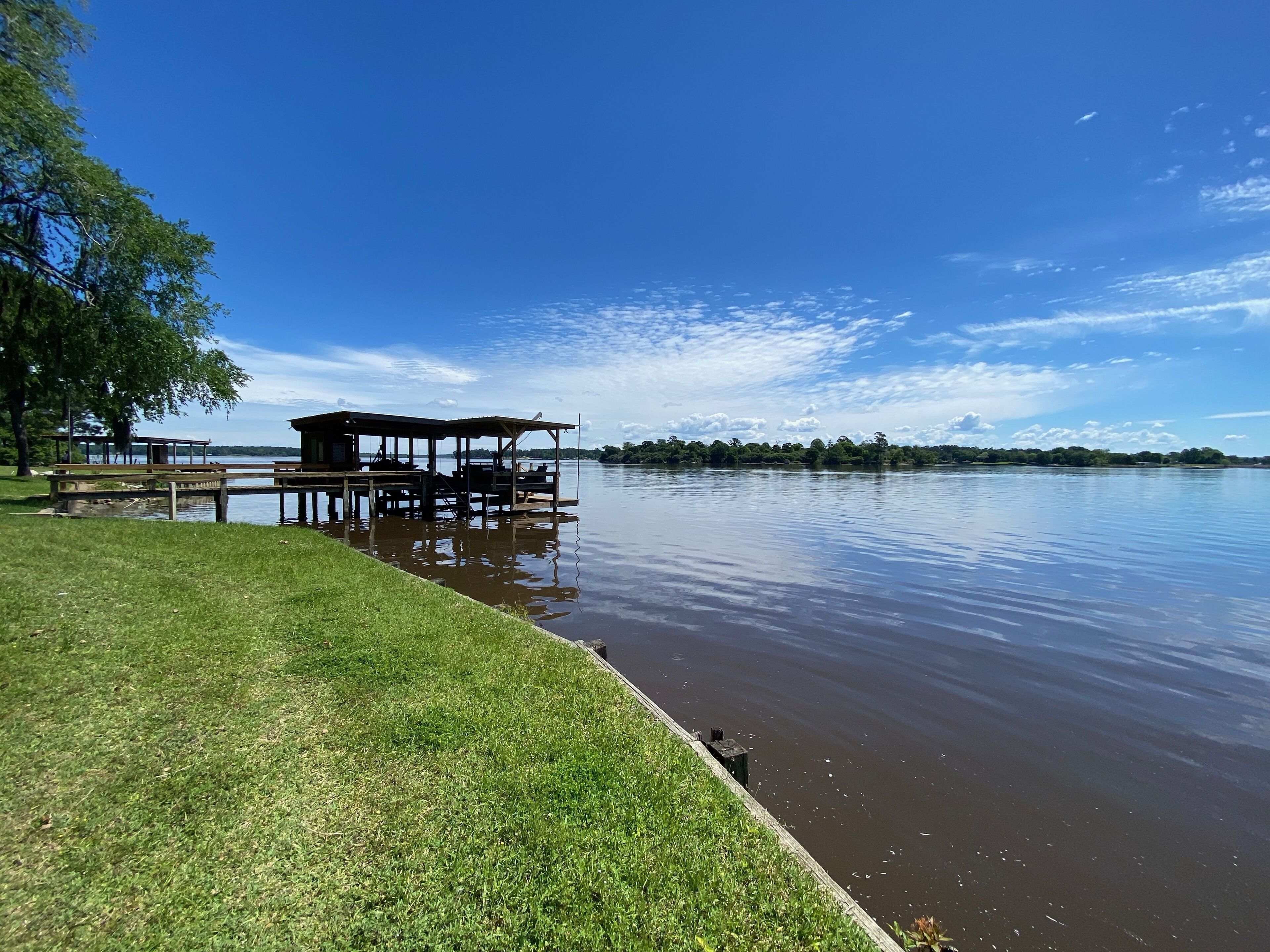 A lakeside dock with a gazebo and picnic tables, surrounded by grassy areas and trees.