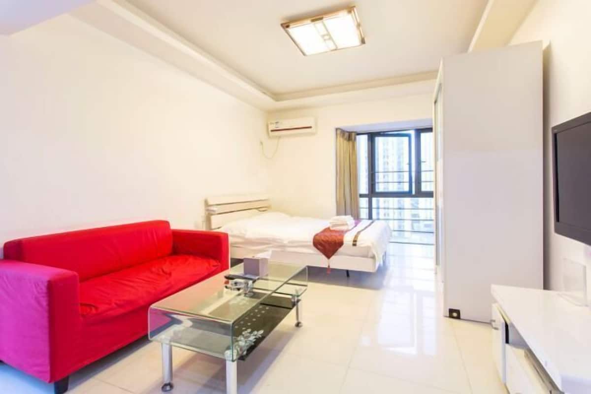 Habitación de hotel con sofá rojo, mesa de centro de vidrio, cama con ropa blanca, televisor y aire acondicionado.