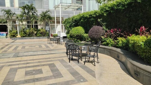 An outdoor patio area with a patterned floor, a round table with chairs, and a variety of plants and shrubs. - Keluowei Hotel (Shenzhen)