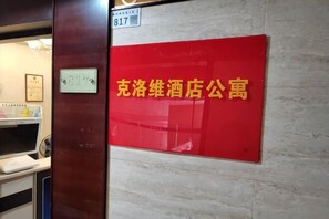 Ein rotes Schild mit chinesischen Schriftzeichen, eine Tür mit einer Nummertafel und ein Teilblick in einen Raum mit einer weißen Theke.