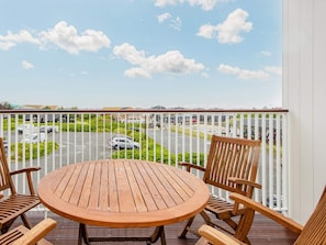 A wooden deck with a round table and chairs, overlooking a parking area and buildings.
