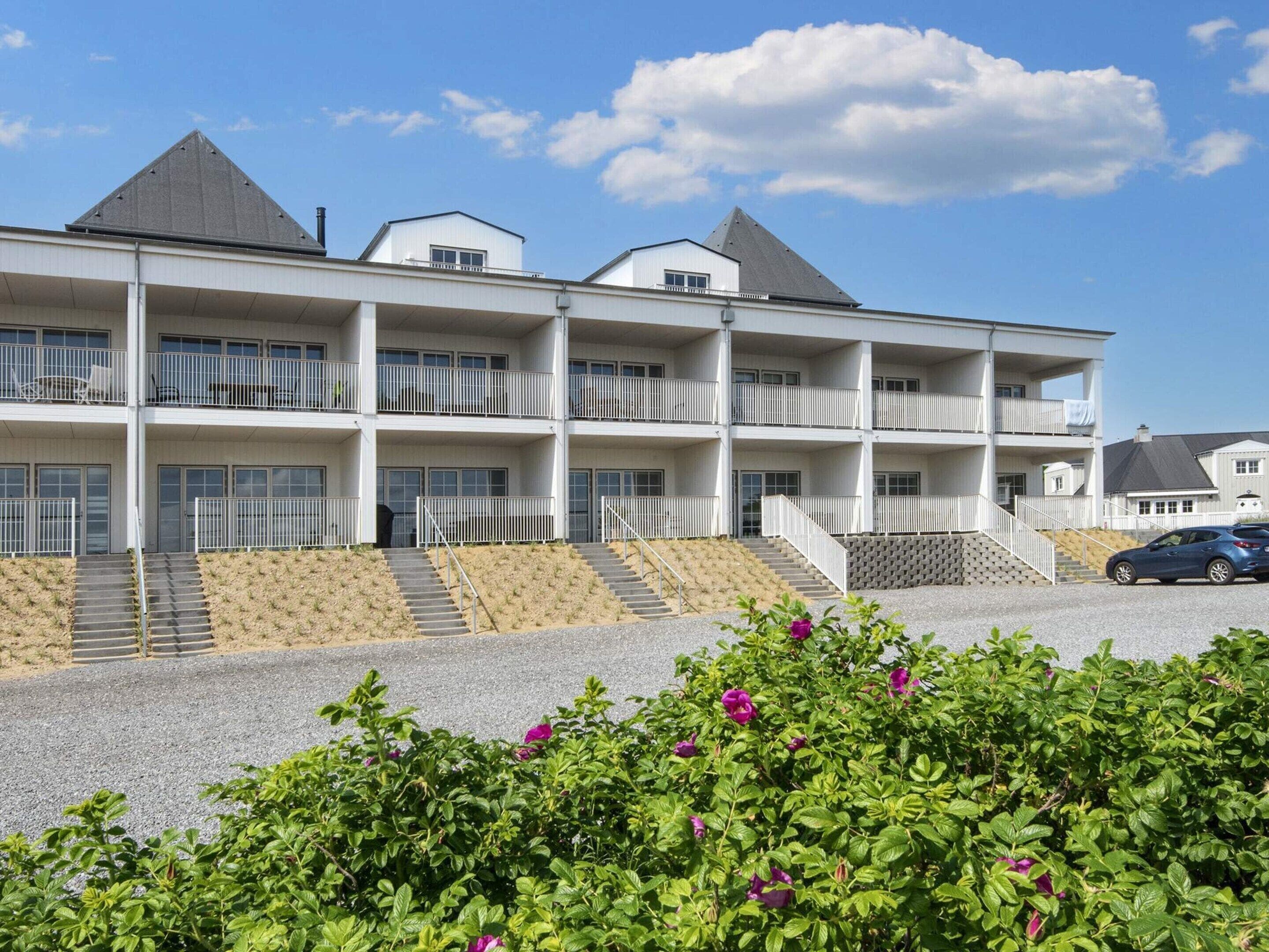 A multi-story hotel with balconies, a parking area, and a landscaped foreground.